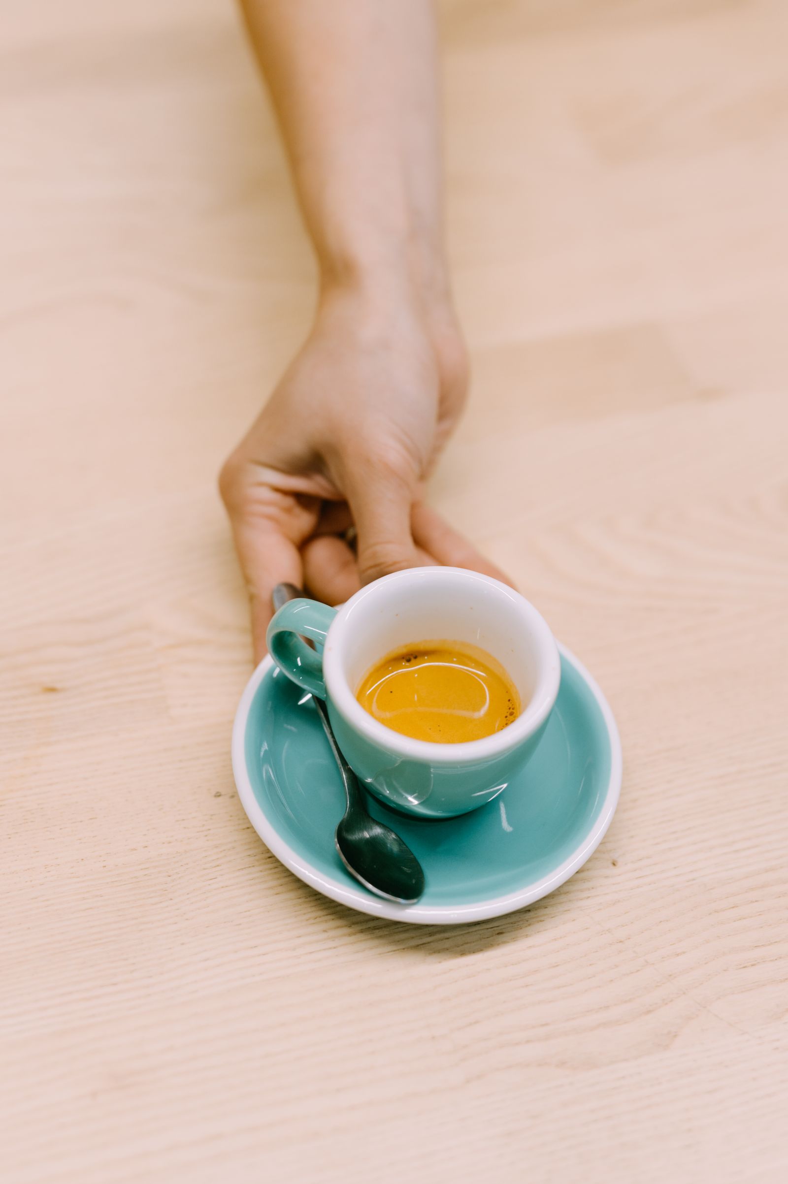 Mão servindo uma xícara de café espresso sobre a mesa de madeira clara