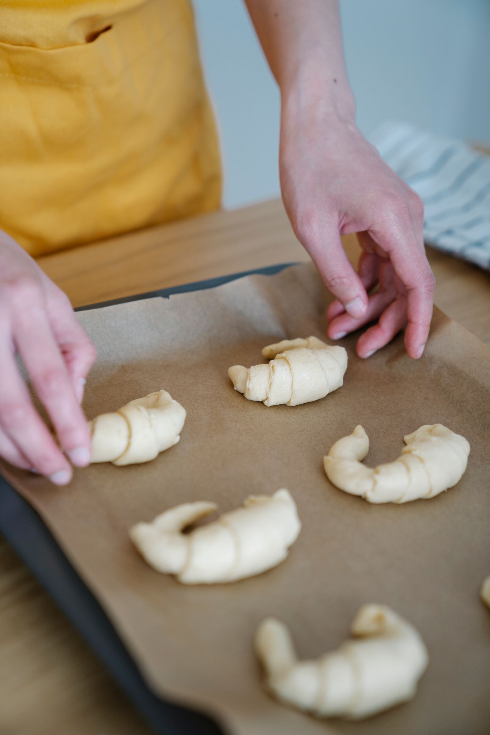 Mãos enrolando croissants crus sobre a assadeira