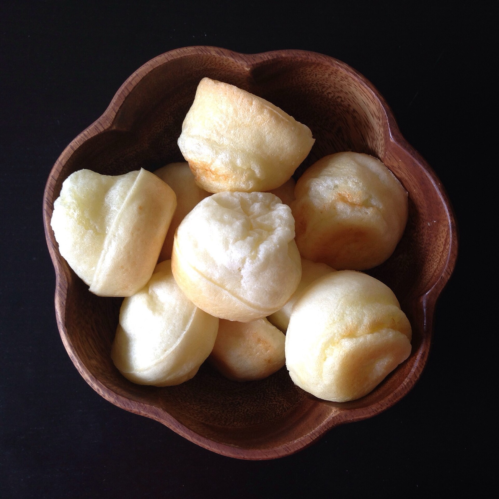 Pães de queijo mineiros dourados servidos em tigela de madeira escura